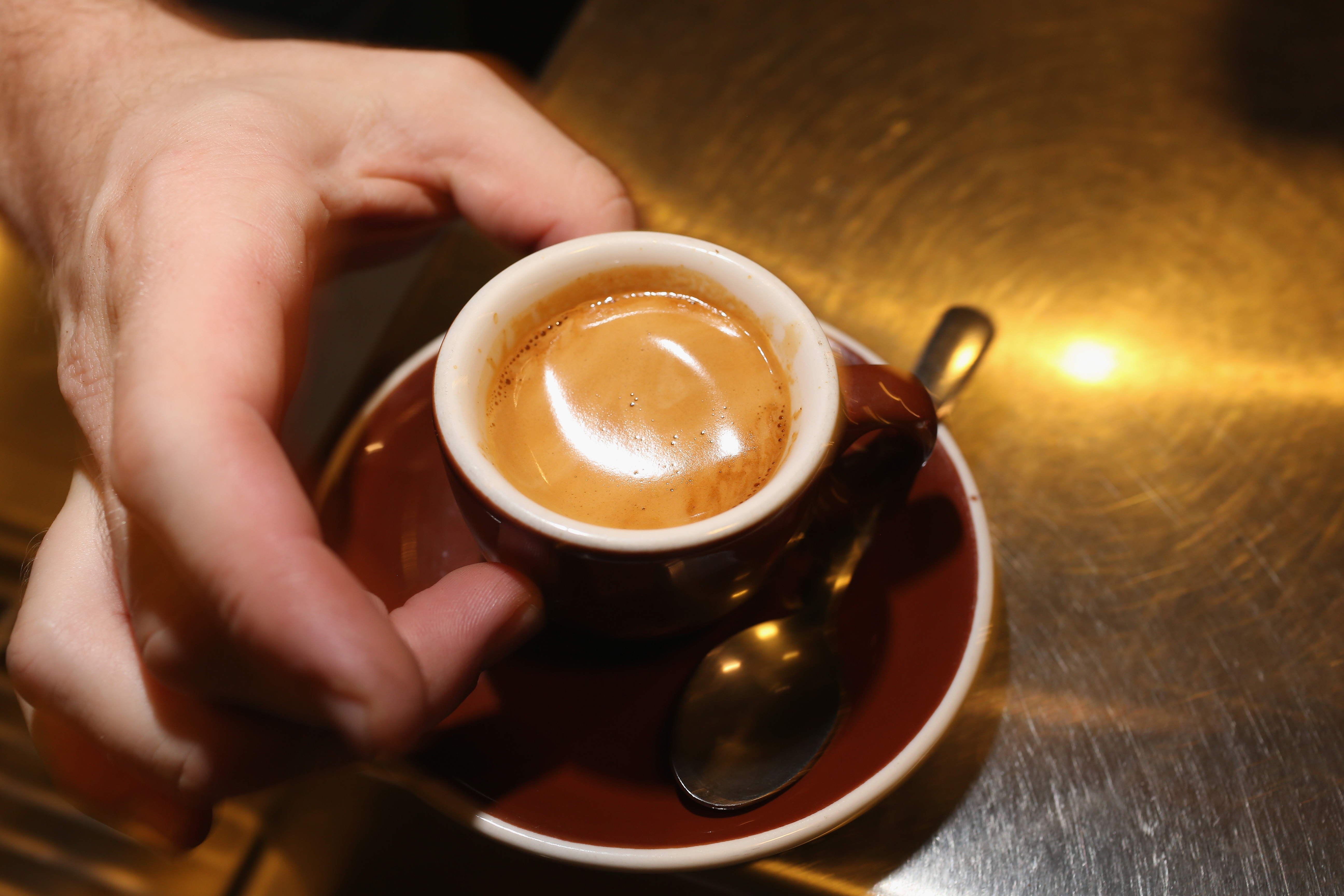 A hand pinches a red cup of espresso between their thumb and middle finger