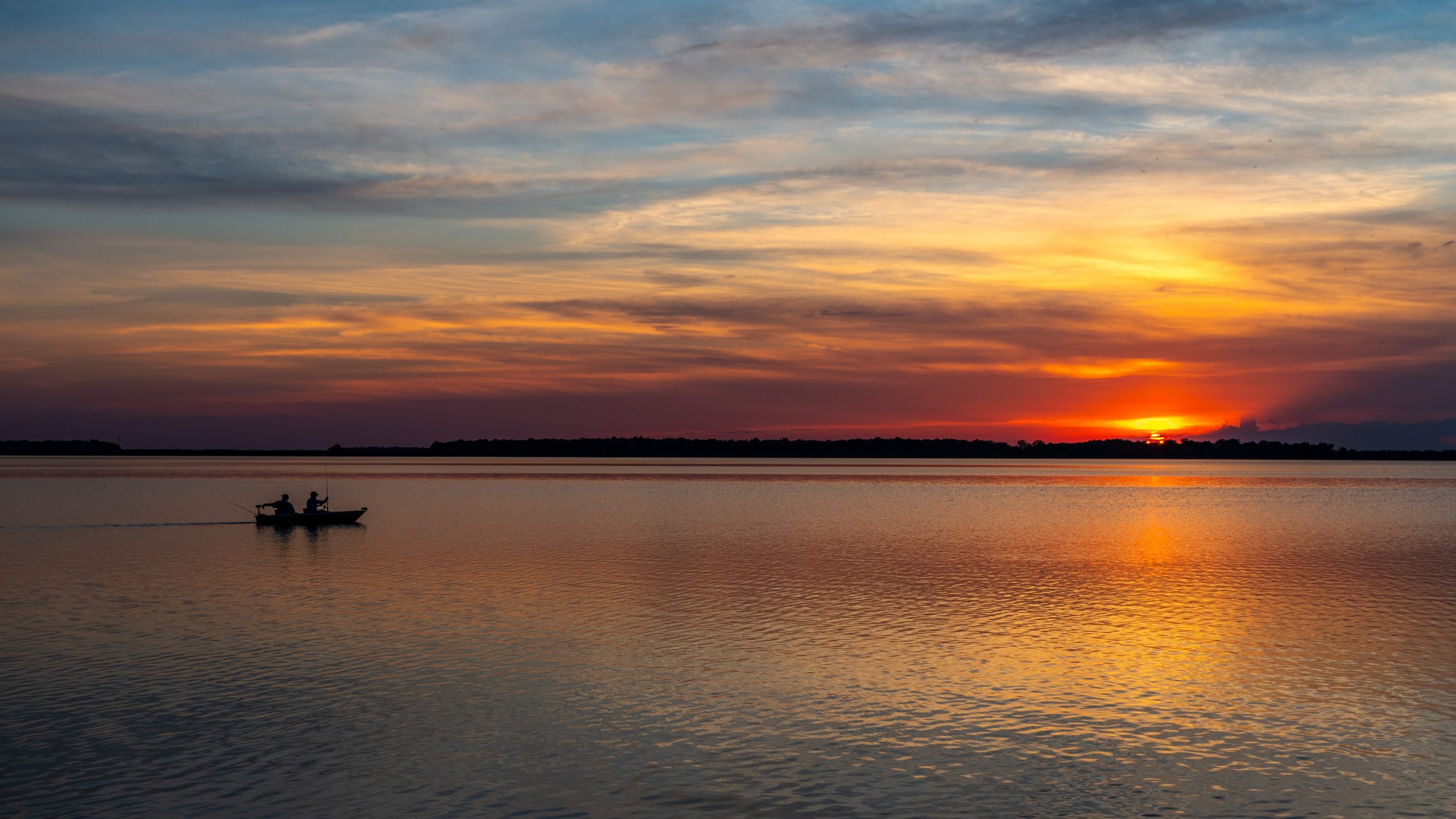 Sun Setting over Lake with Rippled Water, Colorful Sky, and Boat Silhouette