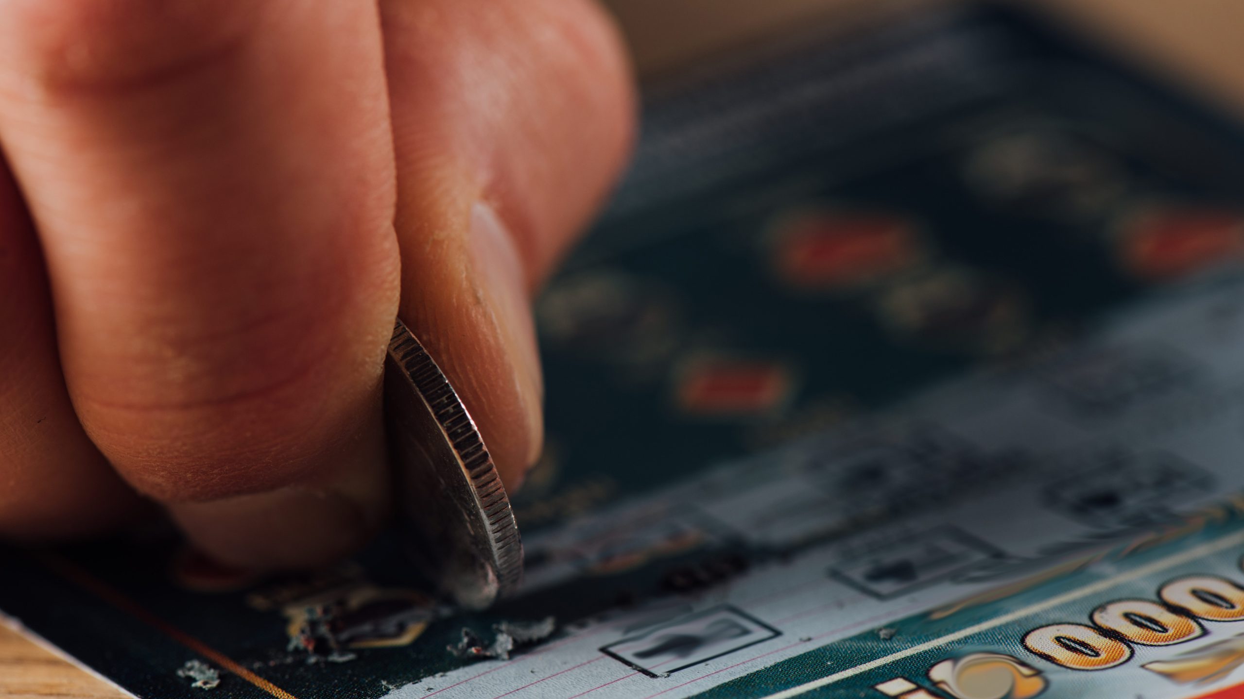 close up view of silver coin in hand of gambler scratching lottery ticket