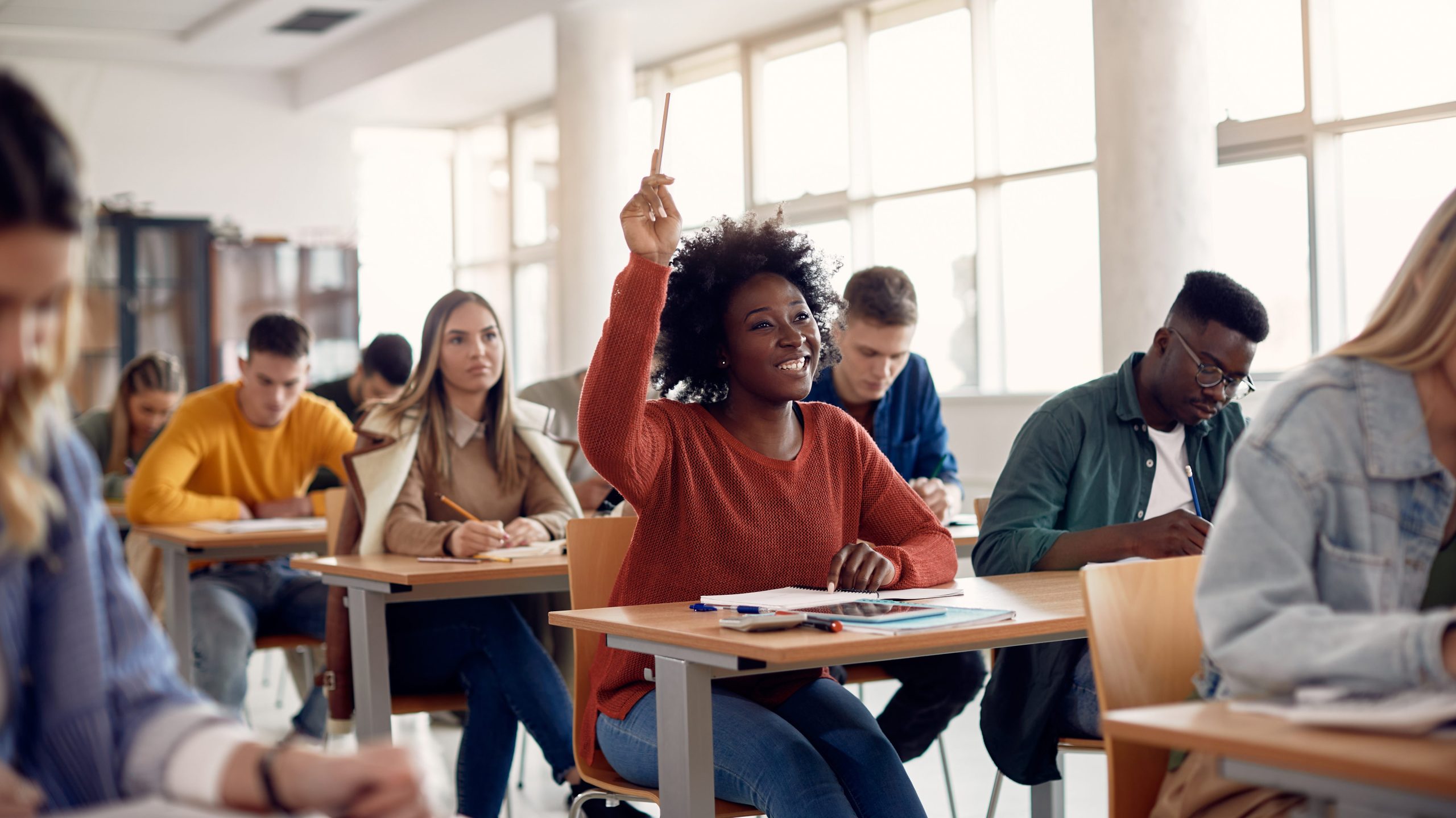 Happy student raising her hand to ask a question during lecture in the classroom.
