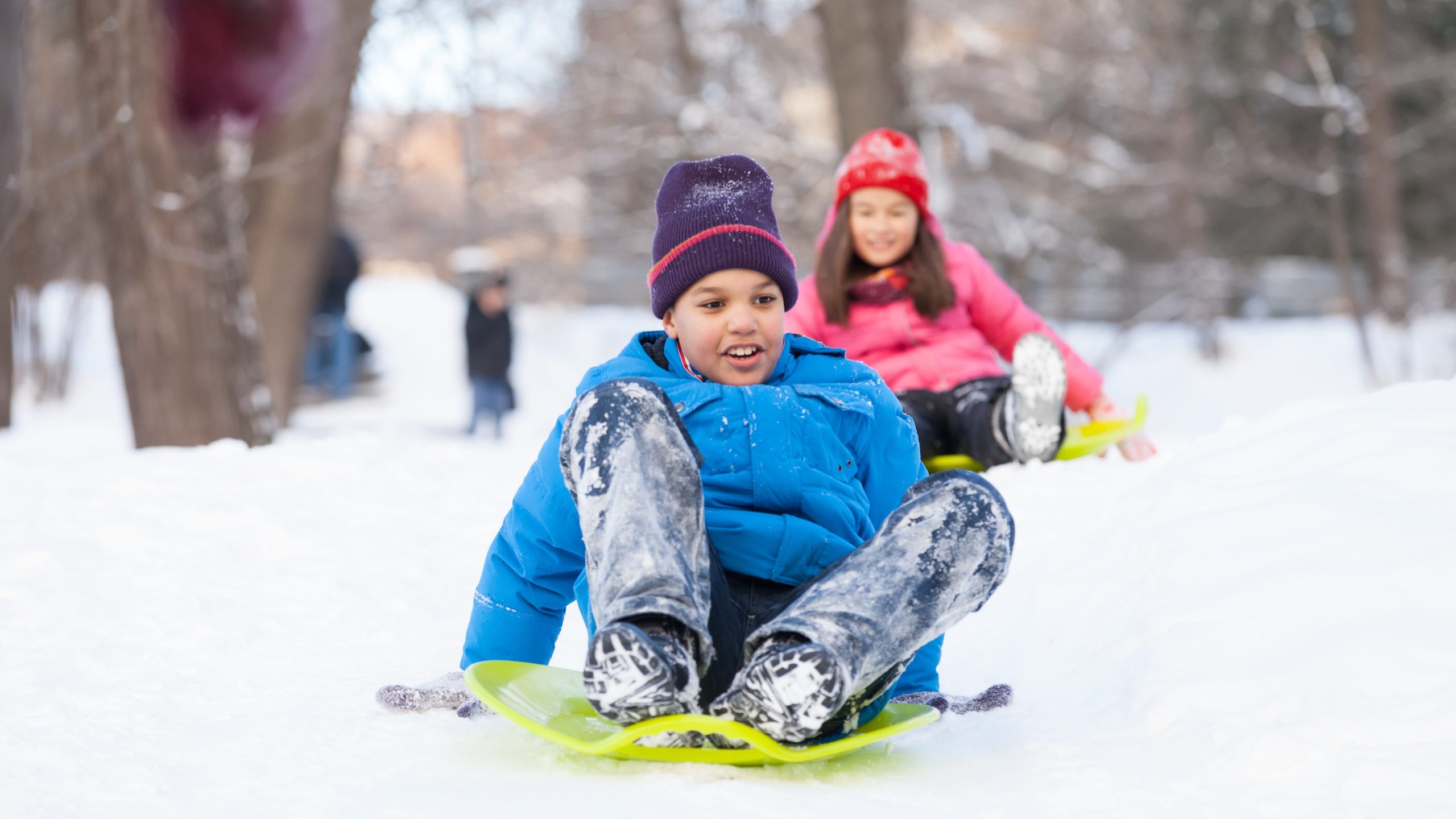 boy and girl sliding on sledges in park. two children sitting on sledges and speeding down
