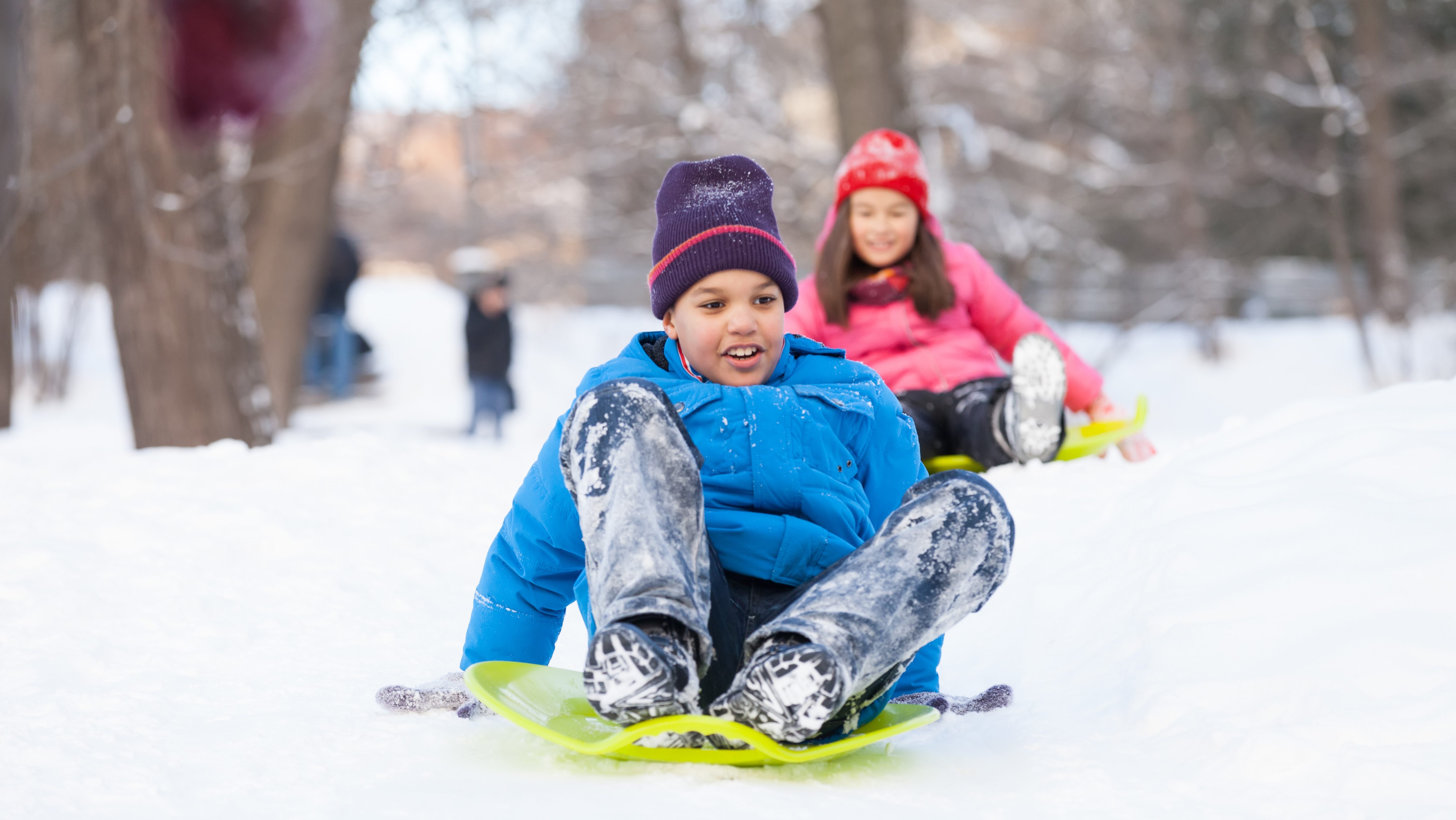 boy and girl sliding on sledges in park. two children sitting on sledges and speeding down
