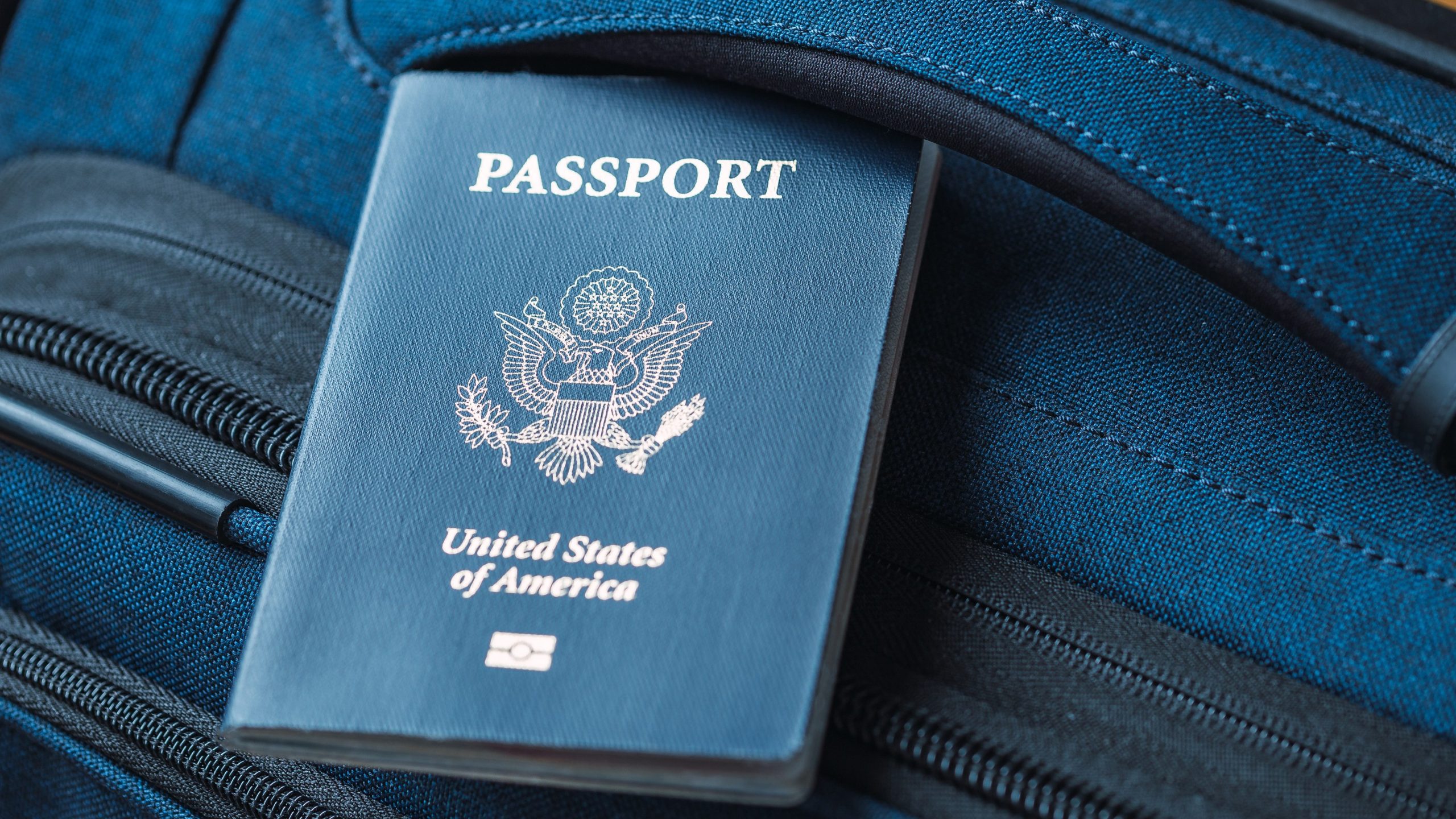 A blue American passport sitting on top of a blue suitcase