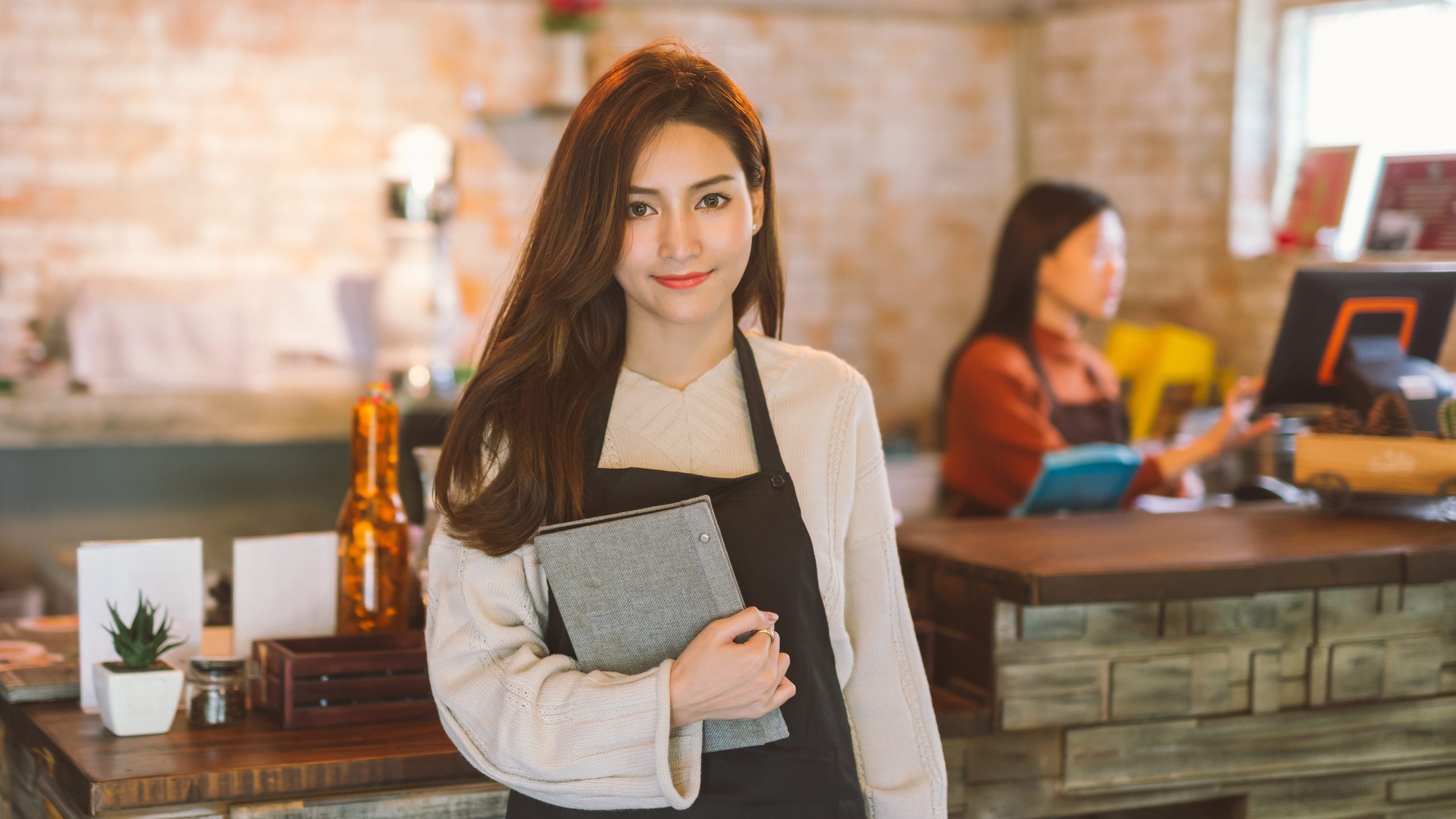 Portrait of waitress holding menu wearing apron and standing in coffee shop.
