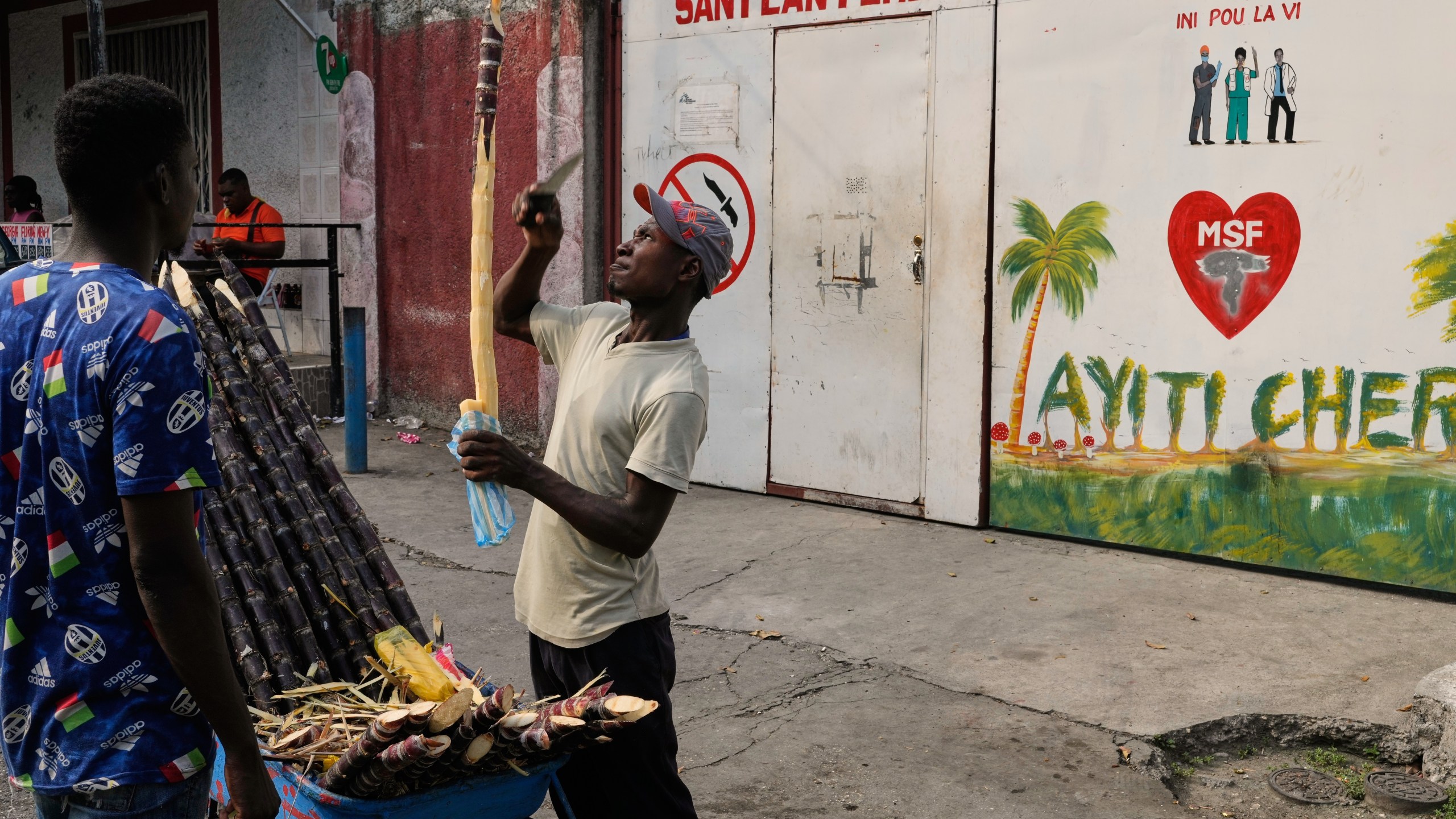 A vendor sells sugarcane next to the entrance of the Doctors Without Borders (MSF) clinic in Port-au-Prince, Haiti, Wednesday, Oct. 15, 2025, after the organization announced the facility’s closure due to ongoing violence. (AP Photo/Odelyn Joseph)