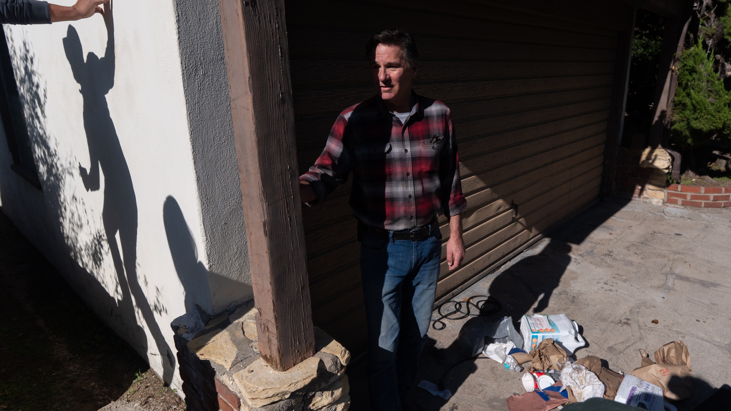 Homeowner Ken Johnson stands outside his house with trash scattered across the driveway after a bear took refuge in a crawl space at his property in Altadena, Calif., Monday, Dec. 1, 2025, as a reporter surveying the scene casts a shadow on a wall. (AP Photo/Jae C. Hong)