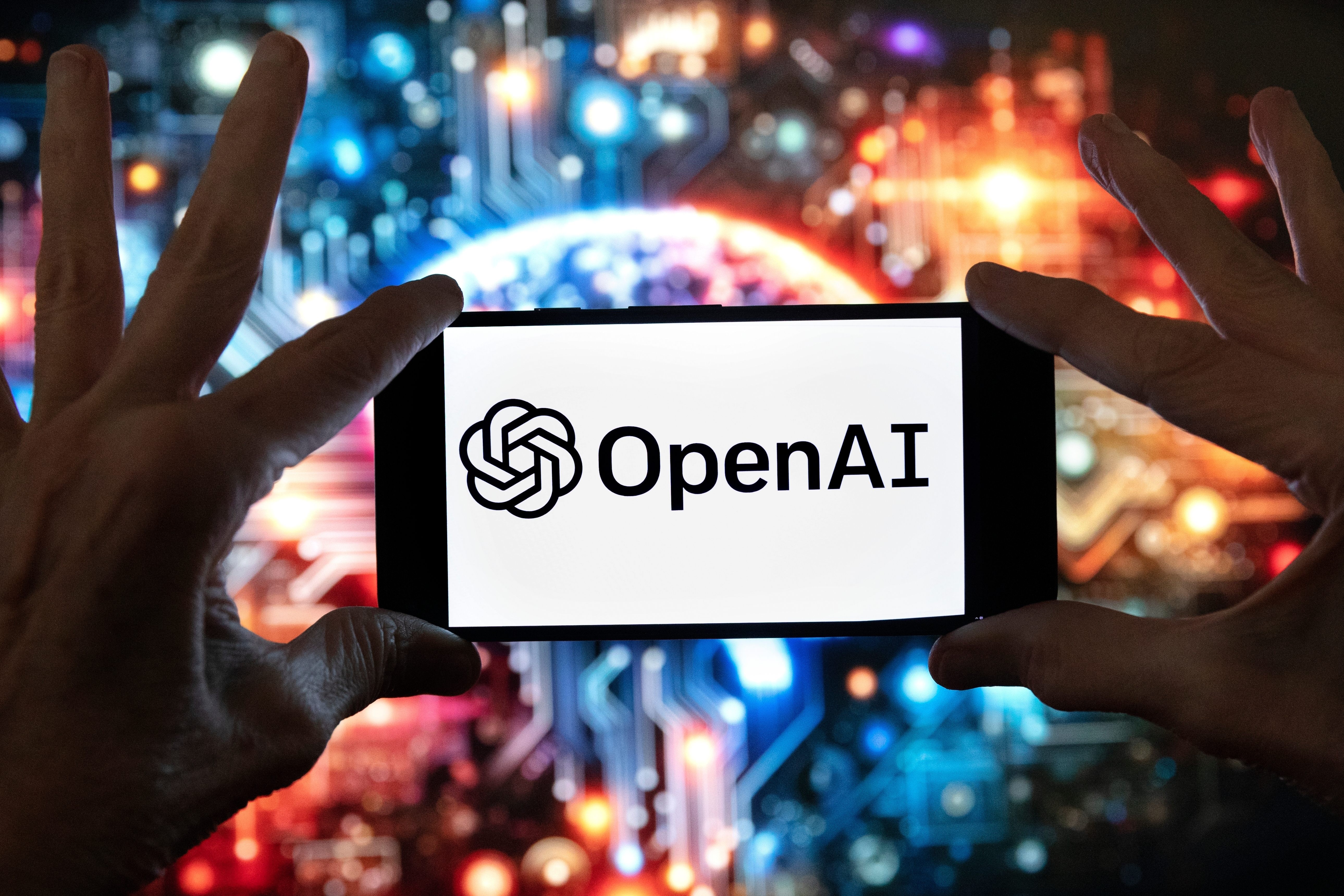 FILE - The OpenAI logo is seen displayed on a cell phone in front of an image on a computer screen generated by ChatGPT's Dall-E text-to-image model, Friday, Dec. 8, 2023, in Boston. (AP Photo/Michael Dwyer, file)