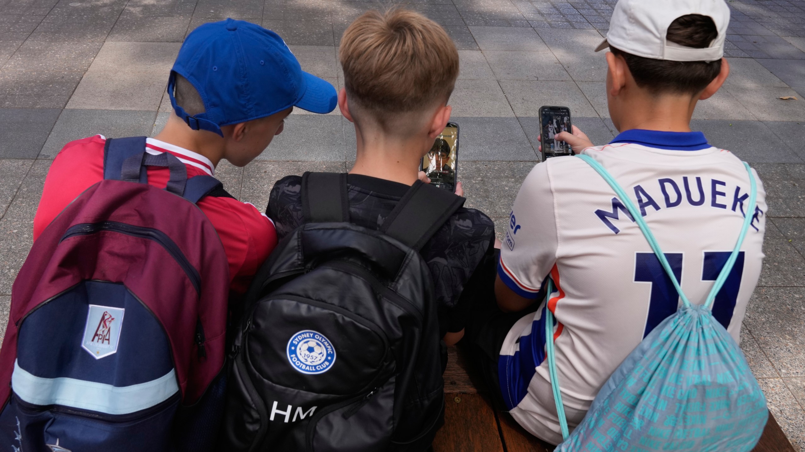 Hugo Winwood-Smith, right, Hardy Macpherson and Edan Abou, left, all 11-years-old, use their phones while sitting outside a school in Sydney, Monday, Dec. 8, 2025. (AP Photo/Rick Rycroft)