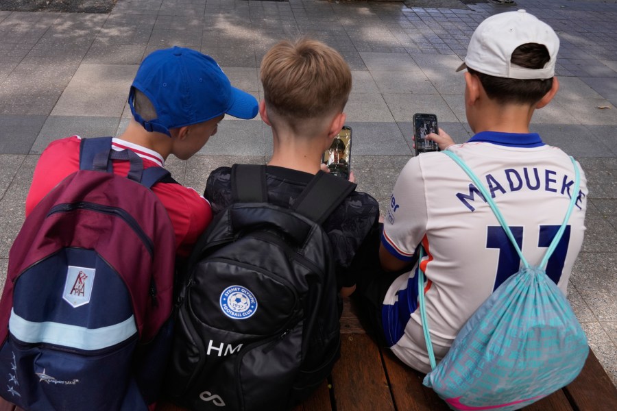 Hugo Winwood-Smith, right, Hardy Macpherson and Edan Abou, left, all 11-years-old, use their phones while sitting outside a school in Sydney, Monday, Dec. 8, 2025. (AP Photo/Rick Rycroft)