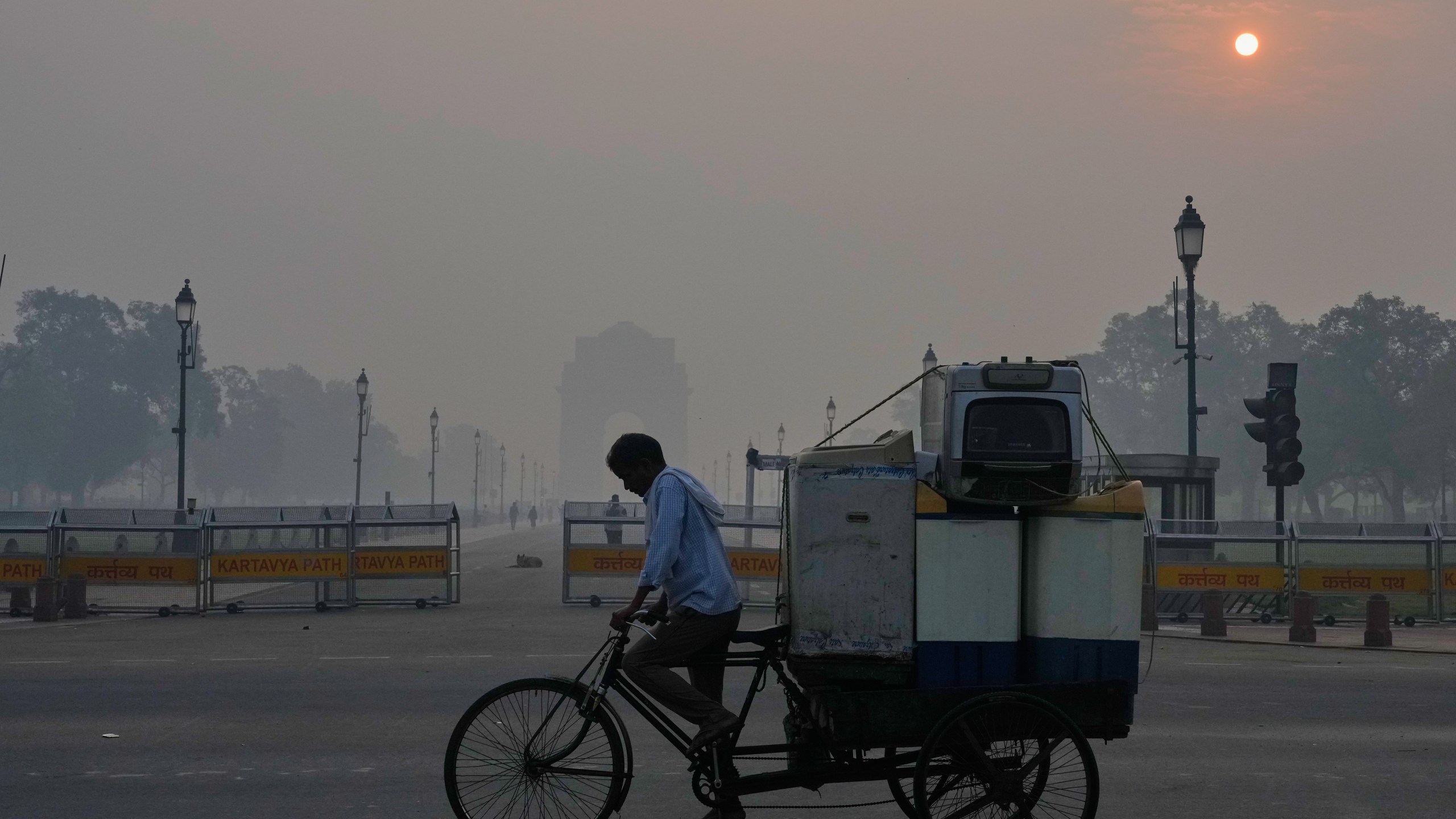 FILE - A cyclist pedals through morning smog near the India Gate monument as he transports used home appliances in New Delhi, India, Oct. 21, 2025. (AP Photo/Manish Swarup, File)